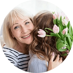 Mature woman hugging her daughter while holding bouquet of flowers